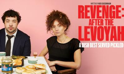 A man and a woman wearing black sat at a table with bagels and pickles on it